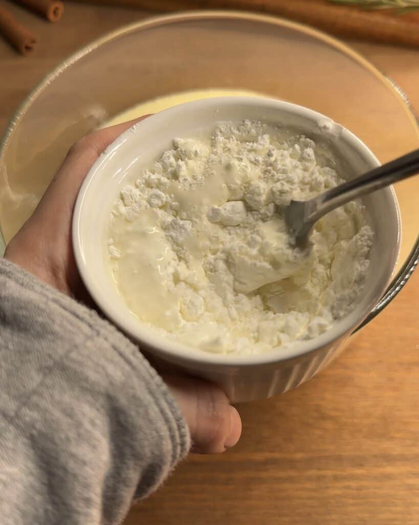 Mixing cornstarch with heavy cream in a bowl to create a smooth and rich filling for Churro cheesecake bars