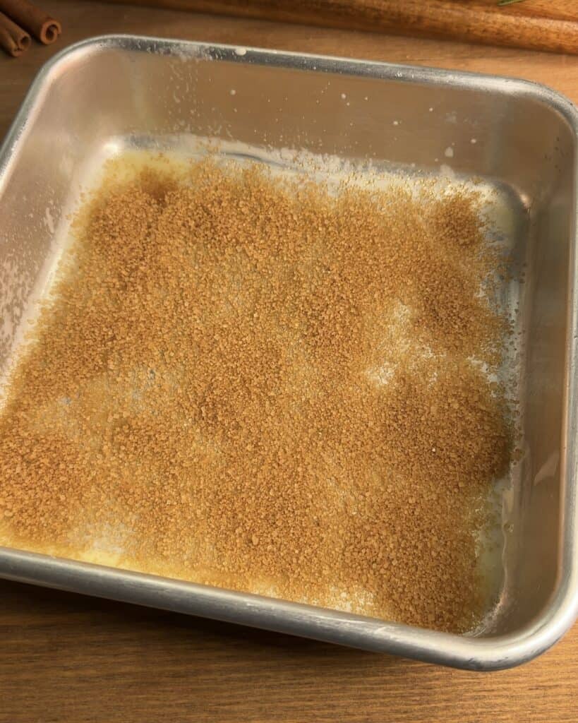 A greased pan with a base of sugar, cinnamon, and melted butter to make Churro cheesecake bars