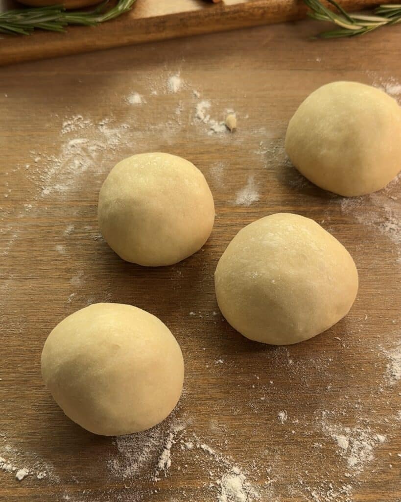 Rolling each dough portion into a smooth ball on a floured surface to prepare Nutella-stuffed brioche