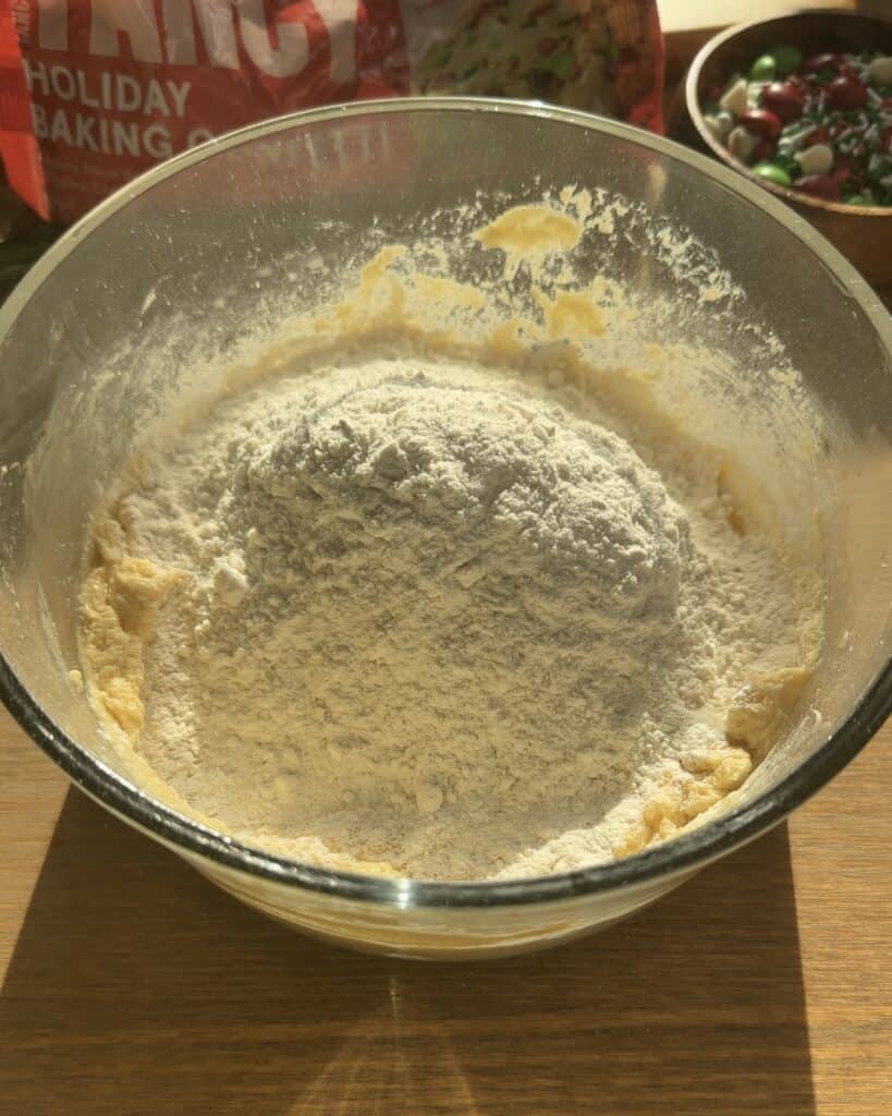 Adding sifted all-purpose flour and baking powder to the cookie batter for Festive Holiday Cookies