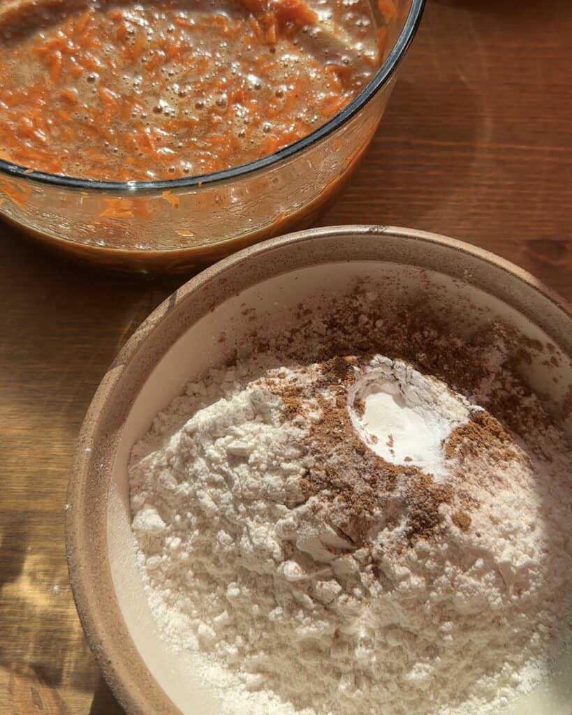 Dry ingredients for carrot cake, including flour, cinnamon, ginger, and baking soda, sifted and ready to be mixed into the batter