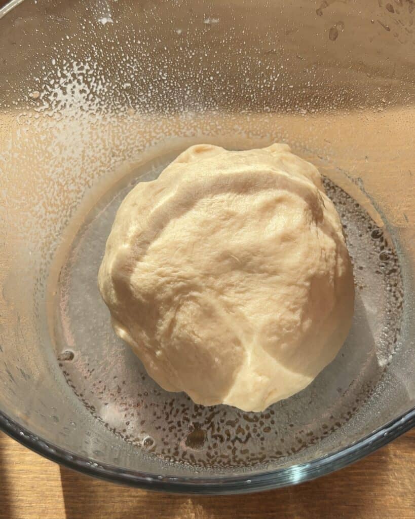 Kneaded dough in a greased bowl, covered and ready to proof, rising to perfection for a soft and fluffy bread.