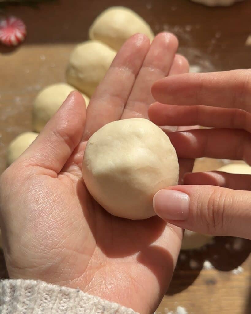 Closing the dough ball around the cheese, carefully sealing it before shaping it into a perfect ball for the pull-apart Christmas tree garlic bread.
