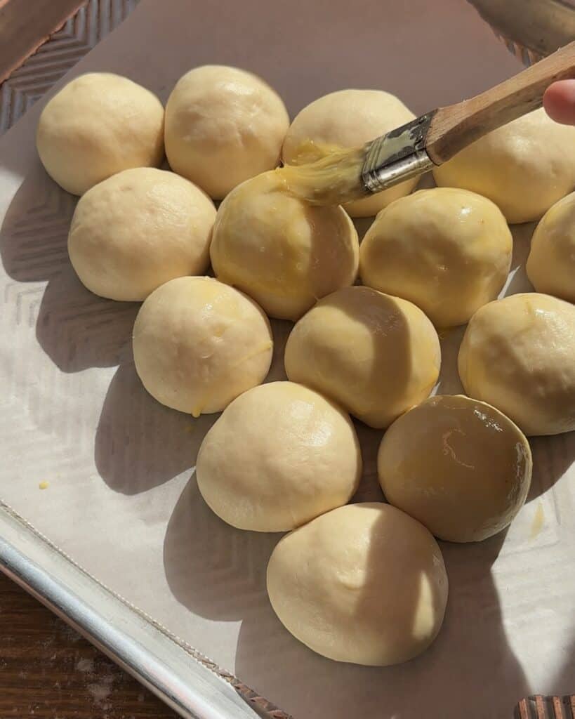 Brushing the shaped dough with an egg wash, giving the pull-apart Christmas tree garlic bread a golden, glossy finish before baking