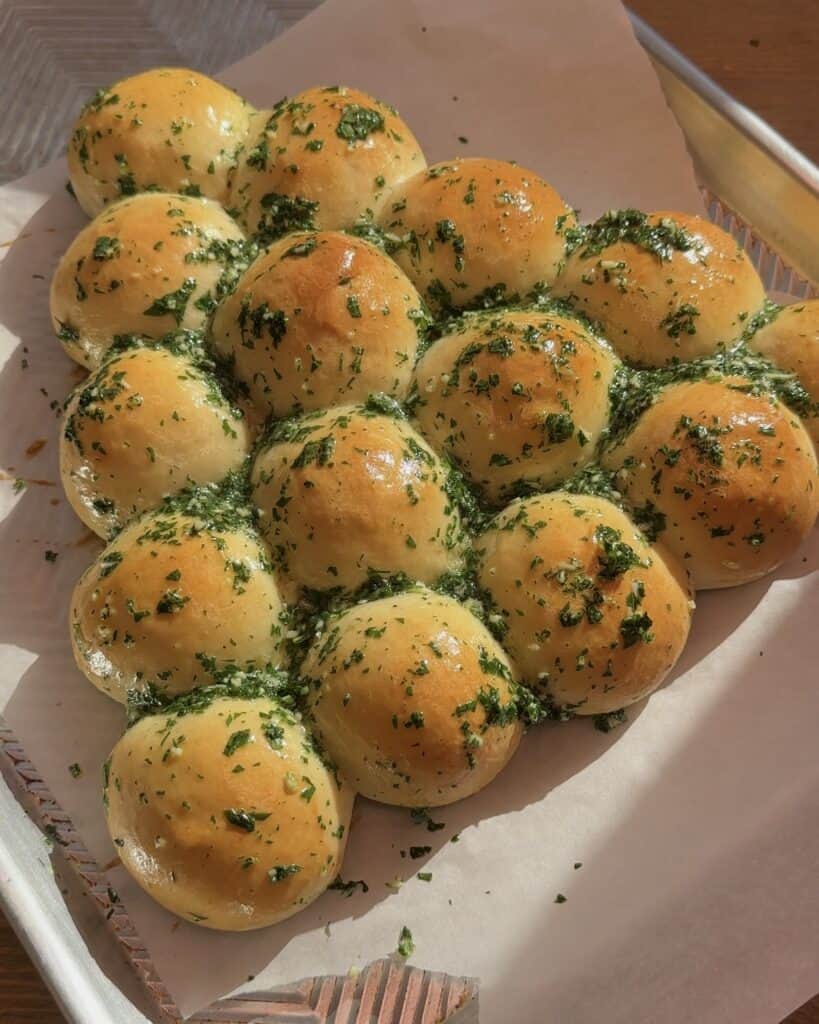 Brushing garlic and parsley butter mixture on top of the baked pull-apart Christmas tree bread, adding flavor and enhancing its festive appearance.