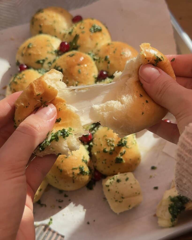 Pulling apart one of the dough balls, revealing the melted cheese inside, showcasing the gooey, cheesy center of the pull-apart Christmas tree garlic bread.