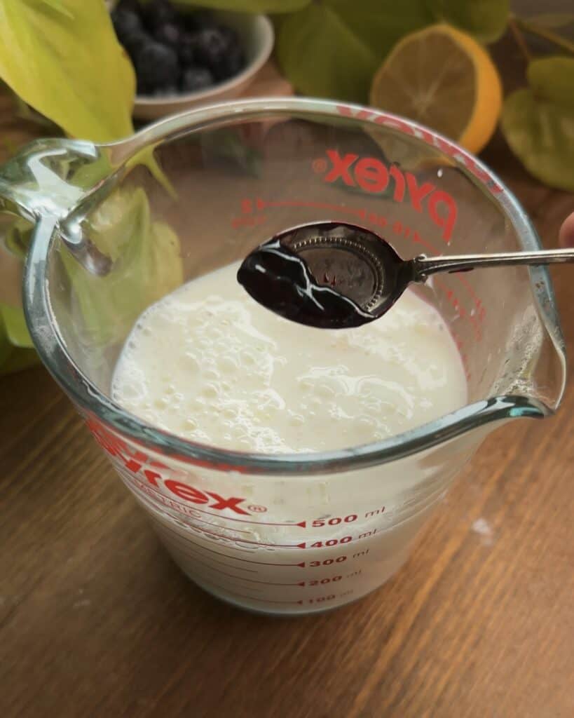 Pyrex bowl with eggs, buttermilk, and red food coloring for making red velvet Nutella pancakes, ready to be whisked together for a vibrant, rich pancake batter.