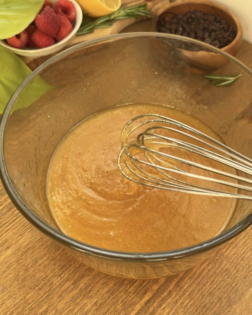 a mixing bowl with a whisk resting inside, showing a smooth and creamy mixture of melted butter combined with sugar.