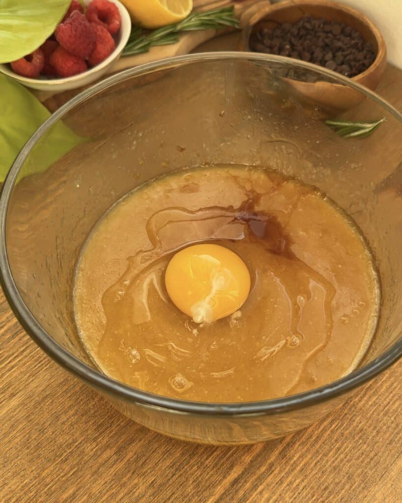 A mixing bowl containing smooth batter of melted utter, sugars with an egg and vanilla extract