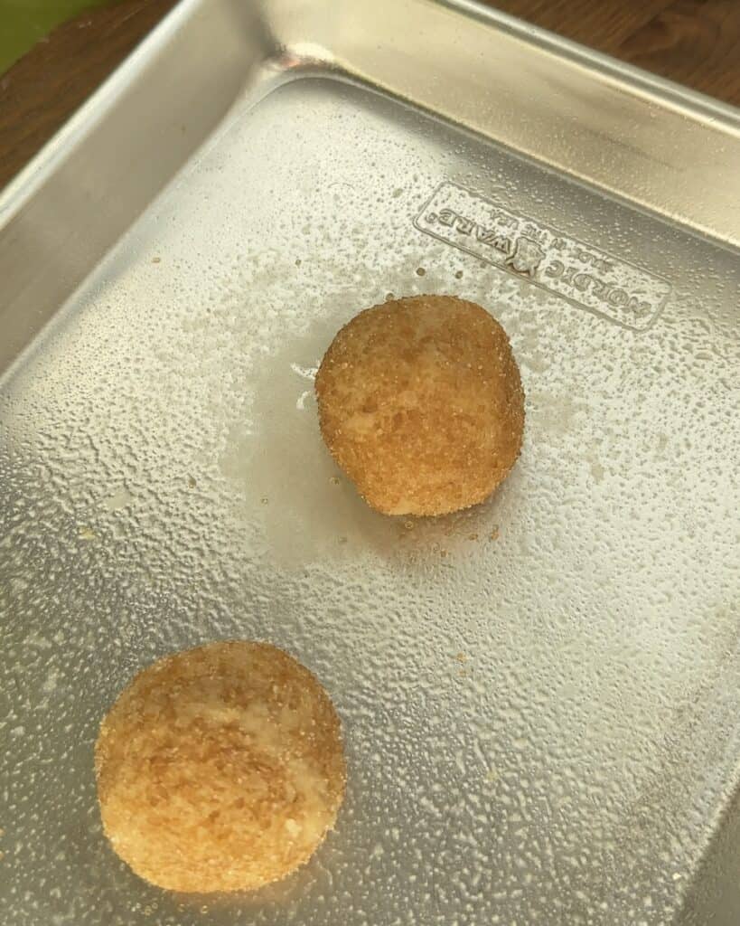 Two snickerdoodle sugar-coated dough balls placed on a greased baking tray, ready to be baked.