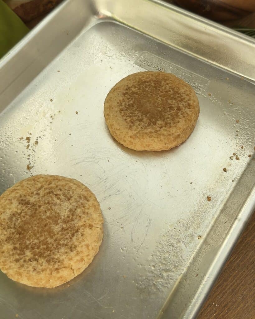 A close up of two freshly baked snickerdoodle cookie resting on a baking pan coated in a sugar mixture