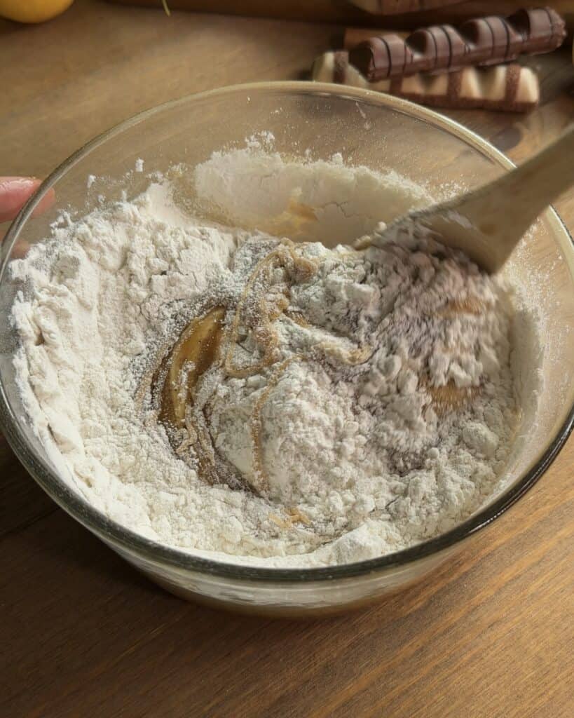 Flour being added on top of the brown butter and sugar mixture, ready to be mixed into the dough for soft and chewy Kinder Bueno cookies.