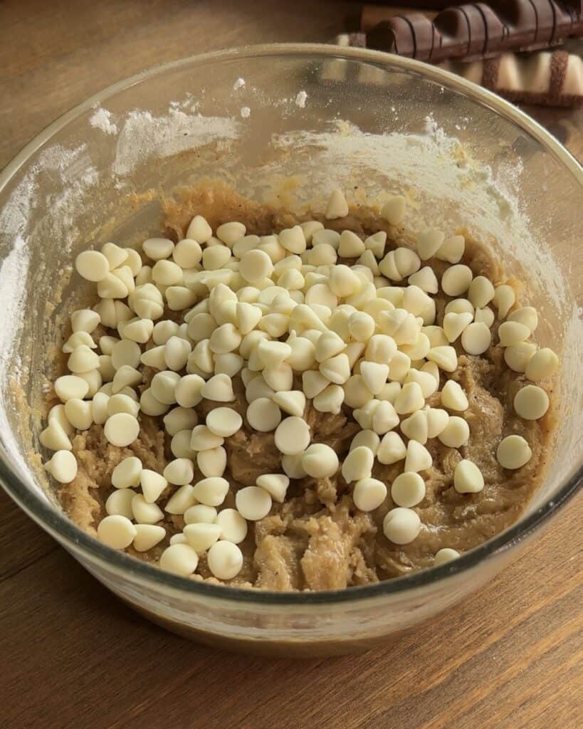 White chocolate chips sprinkled on top of the mixed cookie dough, ready to be incorporated for a delicious Kinder Bueno cookie recipe
