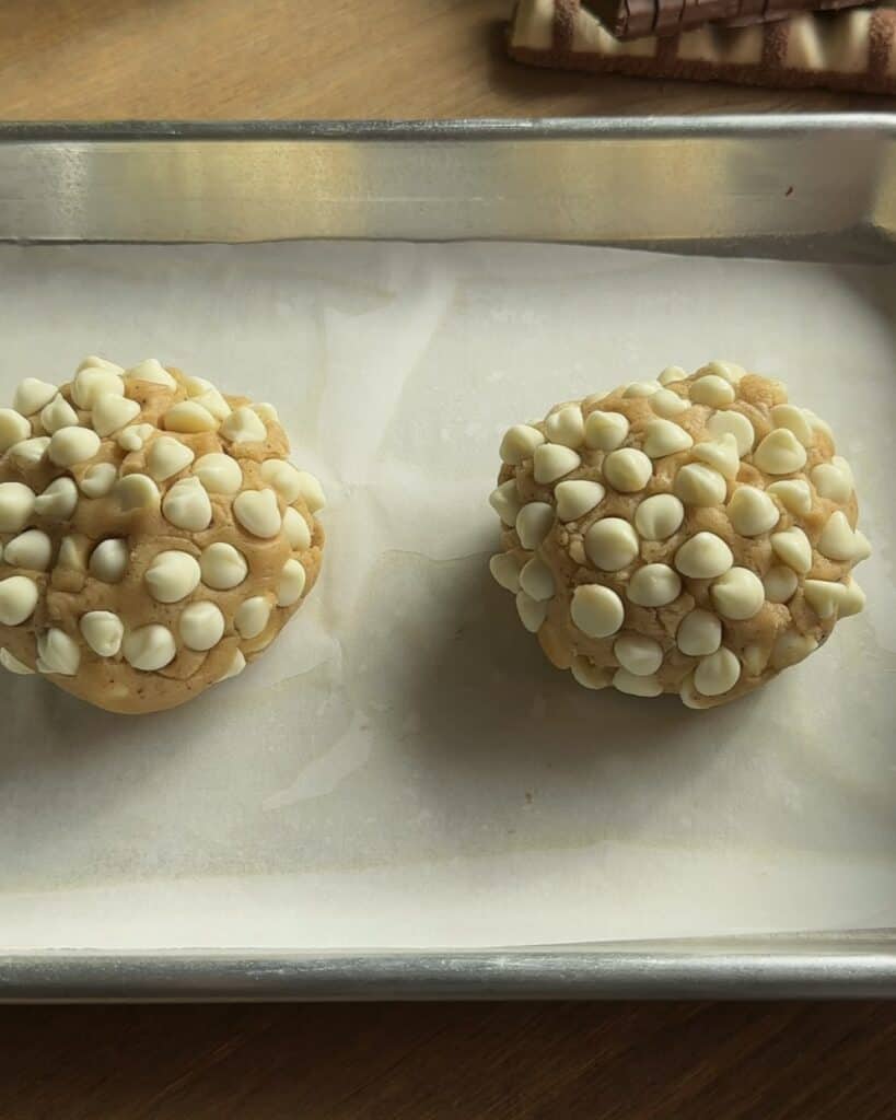 Two freshly prepared Kinder Bueno cookies, topped with white chocolate chips, ready to be baked into soft and gooey treats.