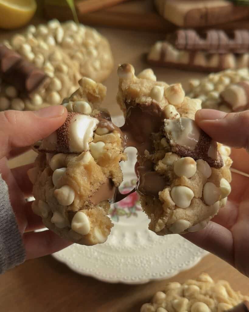 Closeup of a Kinder Bueno cookie split in half, revealing a melted chocolate and hazelnut center, with gooey white chocolate chips throughout.