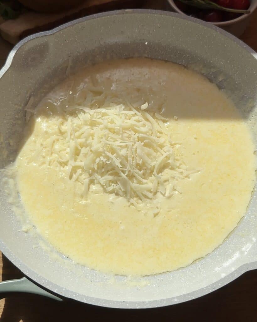 Alfredo sauce simmering in the pan, with melted butter, garlic, cream, and cheese, almost ready to be spread on the chicken pizza crust.