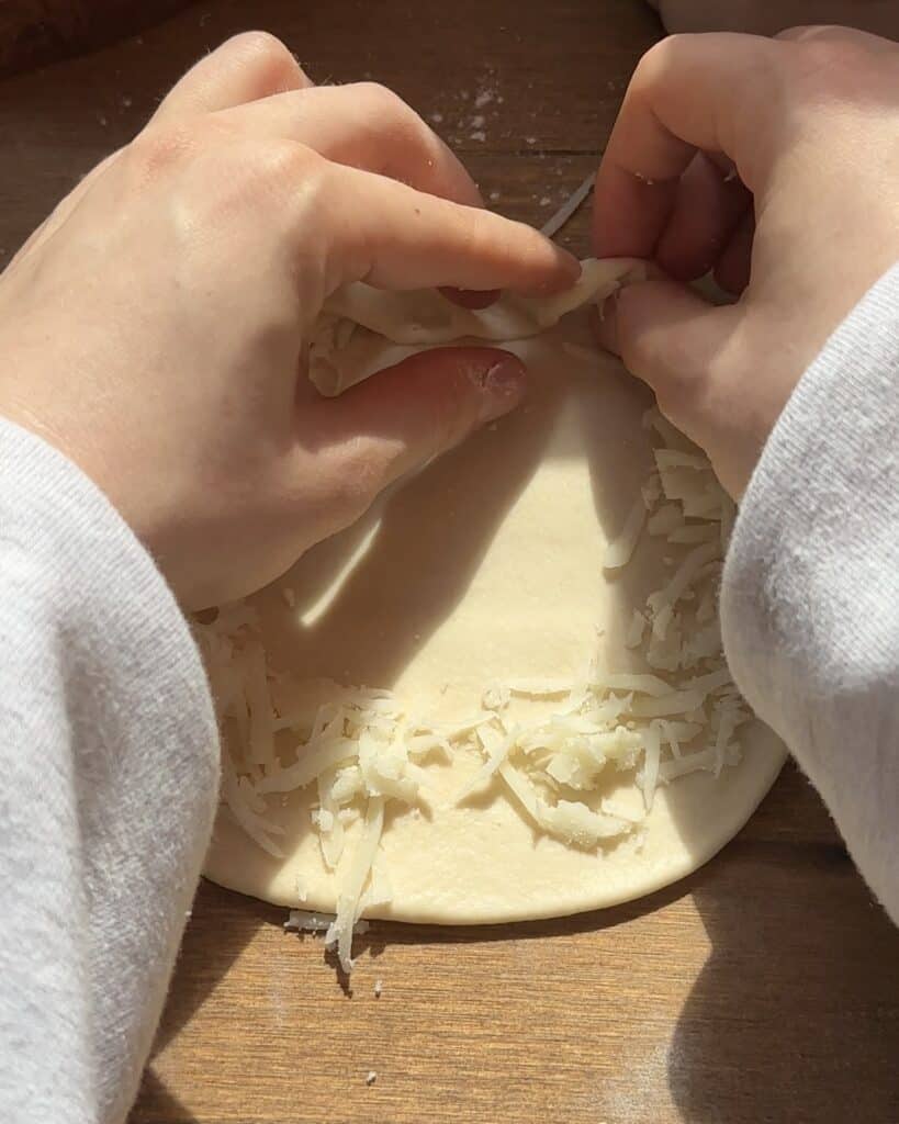 Rolled-out pizza dough shaped into a circle, with mozzarella cheese along the edges, ready to be folded over to create a stuffed crust for a chicken pizza