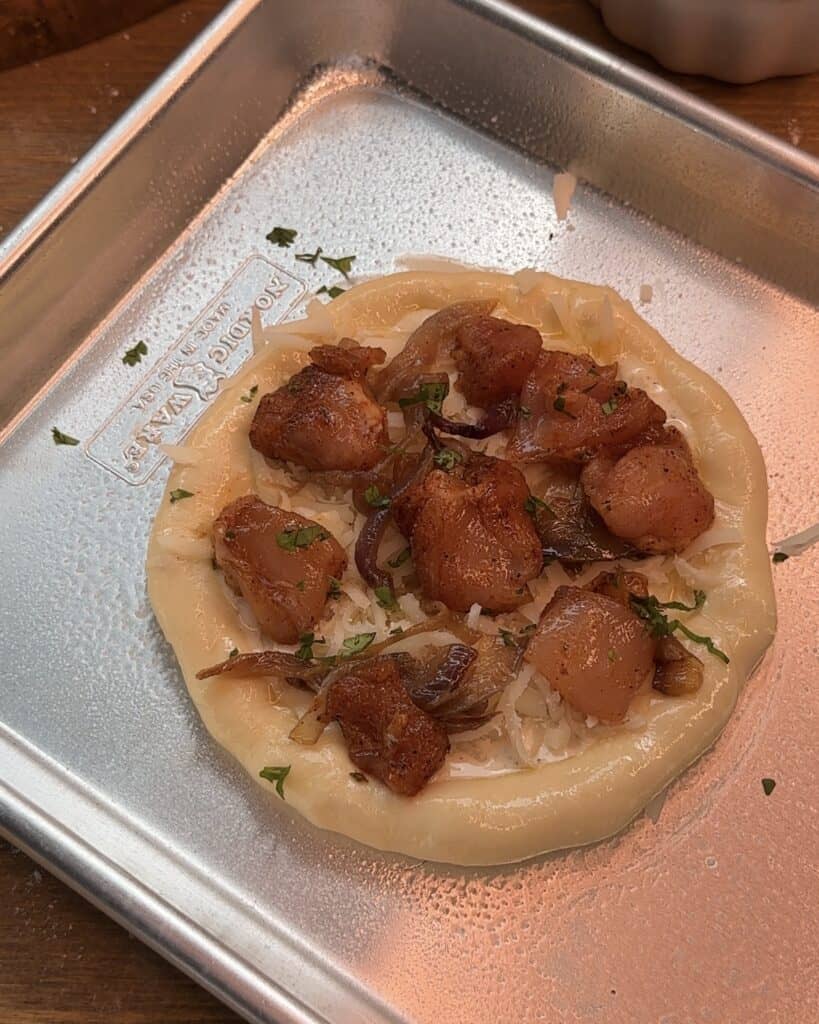 Mini cheesy chicken pizza with Alfredo sauce, caramelized onions, and chicken, ready to be baked, with a cheesy base and fresh toppings
