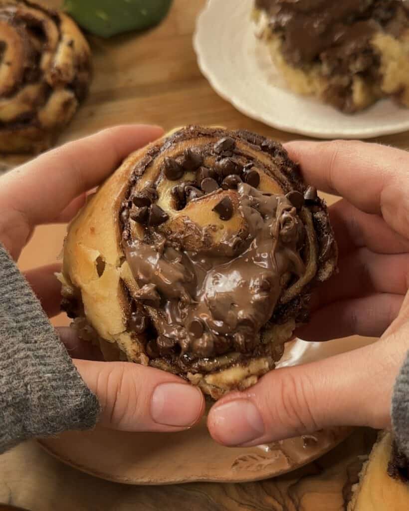 Close-up of a Nutella roll overflowing with gooey Nutella and chocolate chips, about to be torn in half to reveal the rich, chocolate-filled center