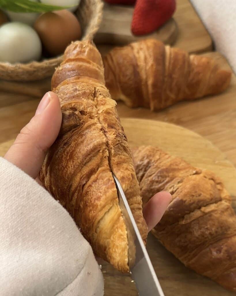 "Cutting the croissant in half horizontally to prepare it for stuffing with pistachio spread and toasted kataifi."