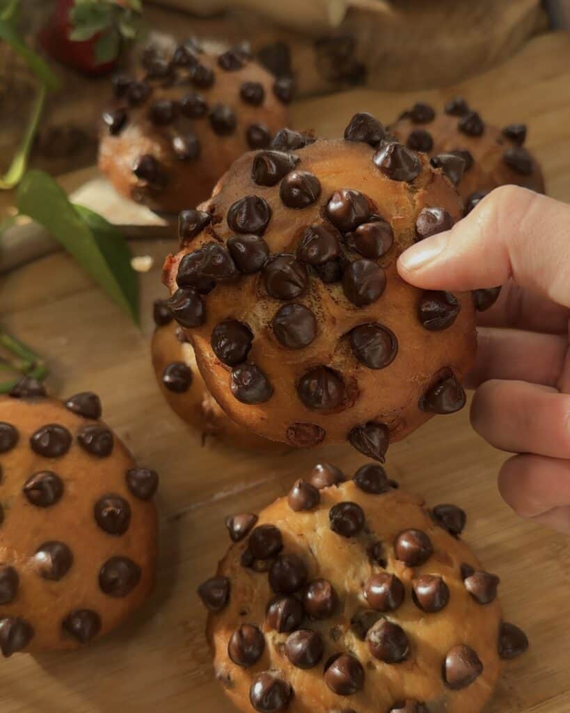 Freshly baked Nutella Bomb Donuts, loaded with chocolate chips, arranged on a board with one held in hand to showcase the soft, fluffy texture and indulgent chocolate filling.