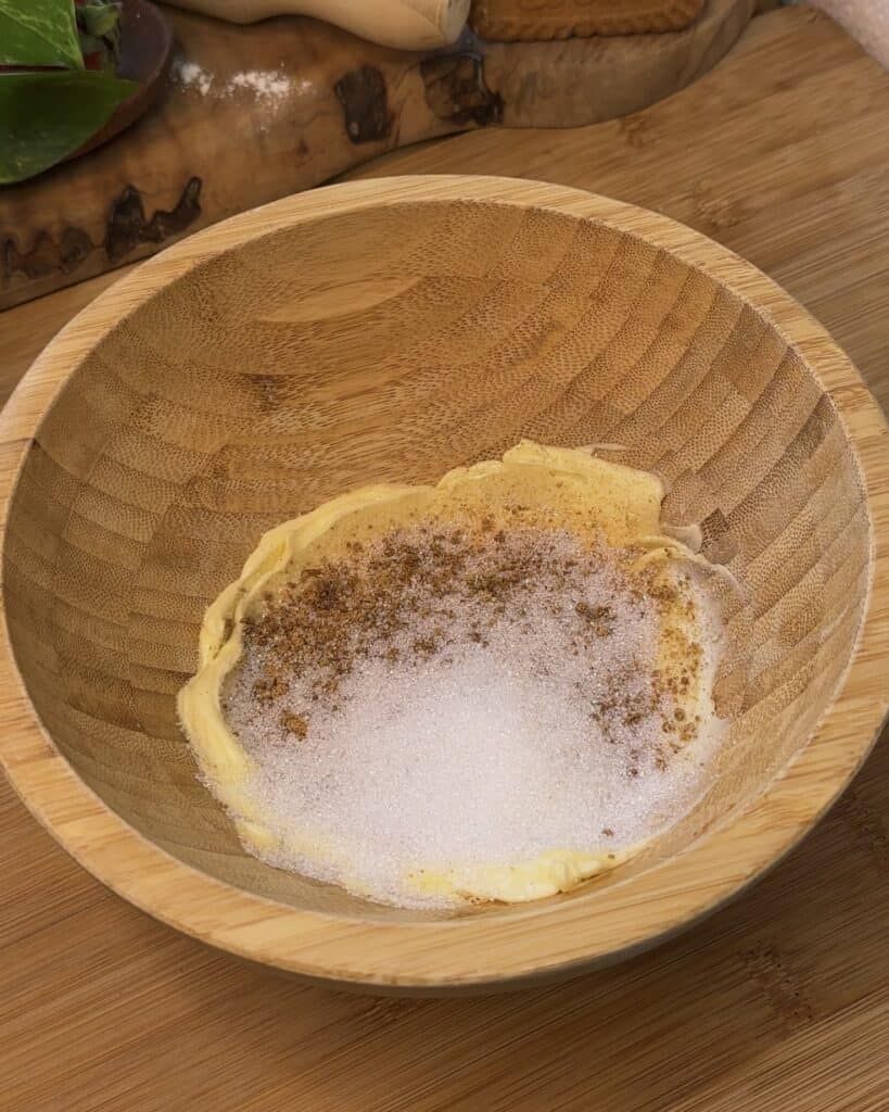 Image of a wooden bowl with soft butter at the bottom, topped with granulated sugar and brown sugar, before being mixed together to create a fluffy texture for the Biscoff marshmallow stuffed cookie dough.