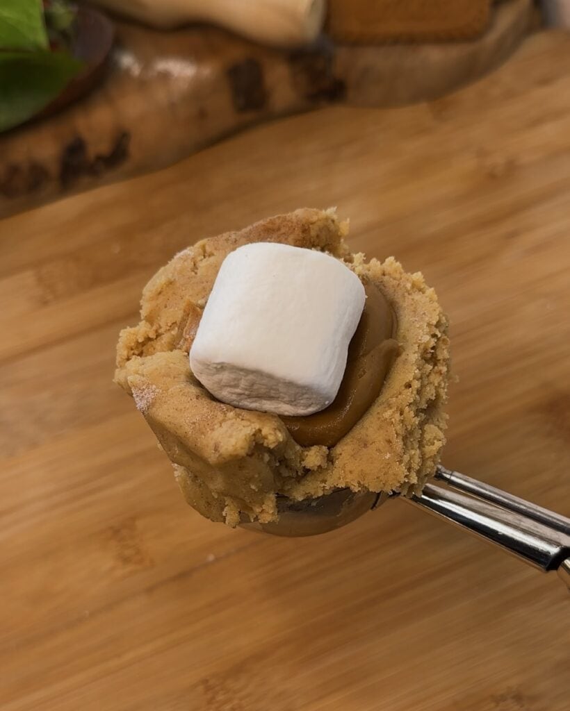 Image of a cookie scoop with Biscoff spread in the middle and a marshmallow before closing it with more cookie dough, preparing the perfect stuffed Biscoff marshmallow cookie.