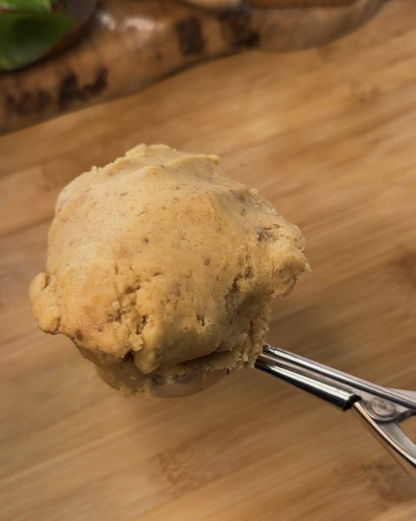 Image of a cookie scoop with Biscoff spread and marshmallow in the center, after being closed with more cookie dough on top