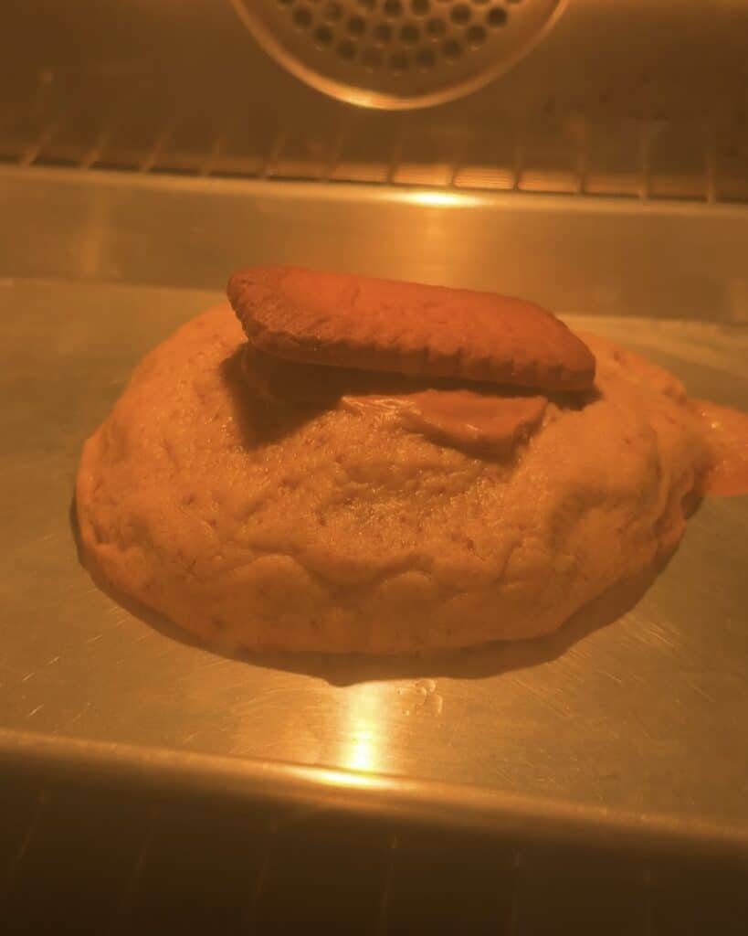 Image of a single-serve Biscoff stuffed cookie baking in the oven, with the dough turning golden and the edges slightly crisp, showcasing the perfect texture of the Biscoff marshmallow stuffed cookie.
