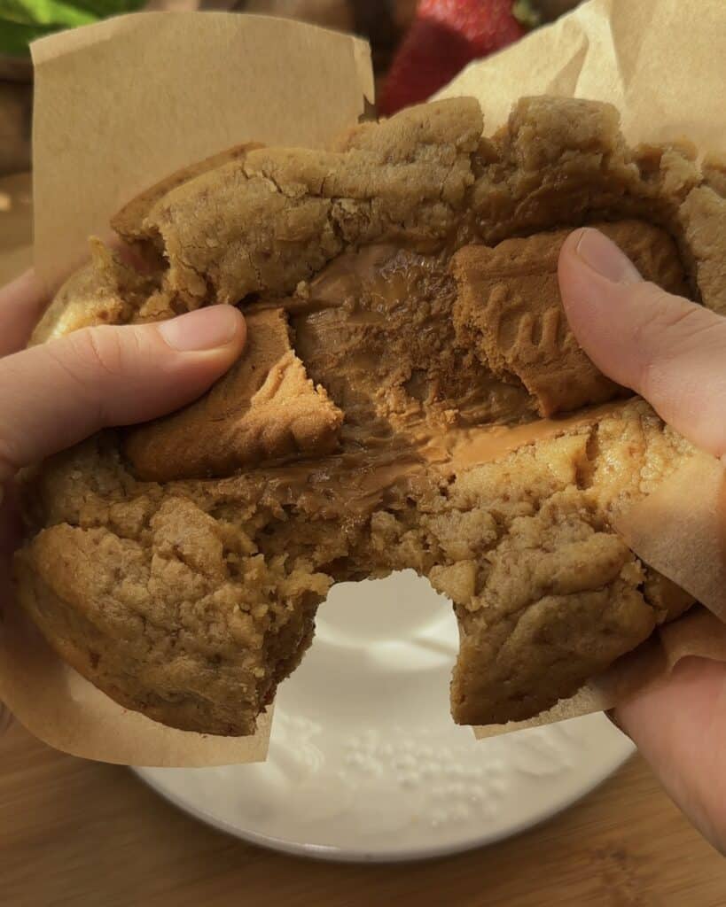 Image of a single-serve Biscoff stuffed cookie being opened in half, revealing the gooey interior with stretchy marshmallow and Biscoff spread, highlighting the delicious, indulgent filling.
