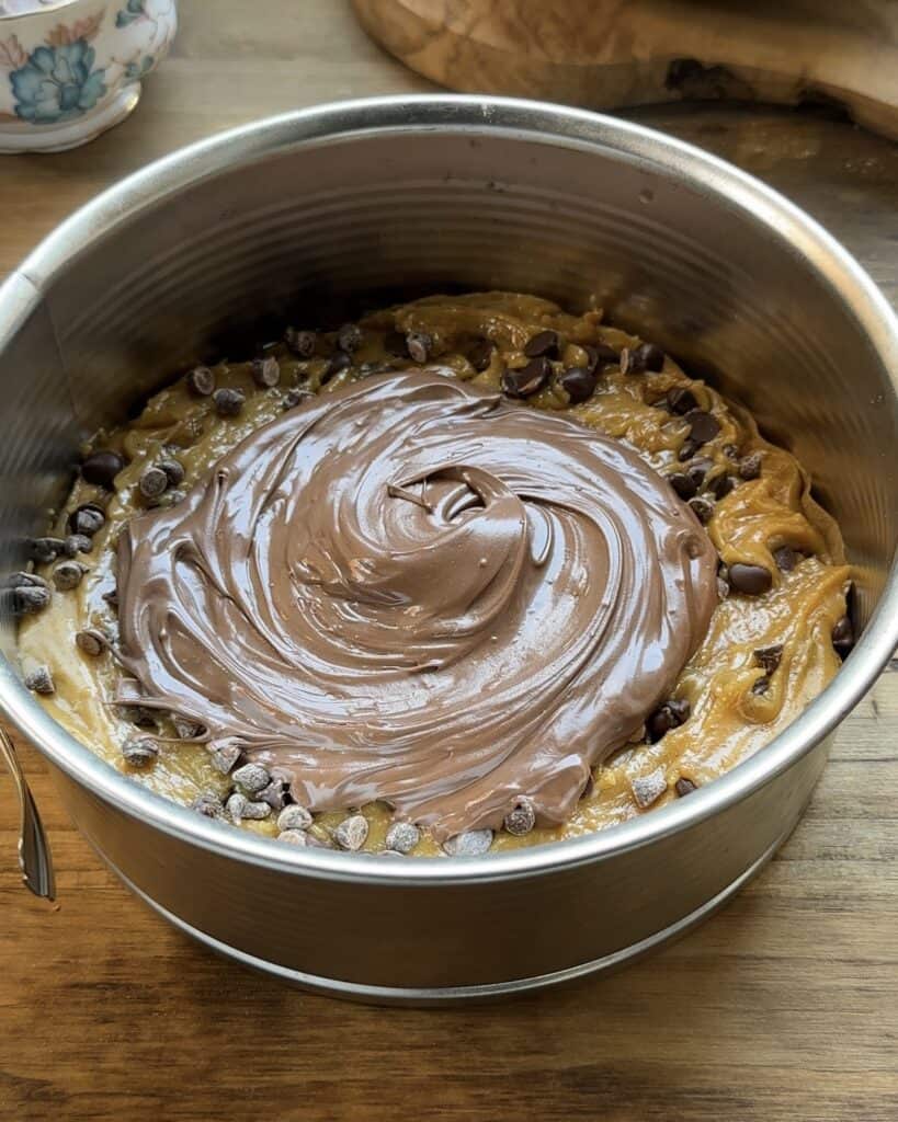 One layer of cookie dough with a generous spread of Nutella in the center, ready to be topped and baked