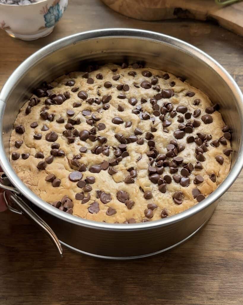 Freshly baked cookie pie straight out of the oven, still in the dish, with gooey chocolate chips scattered throughout, looking golden and delicious