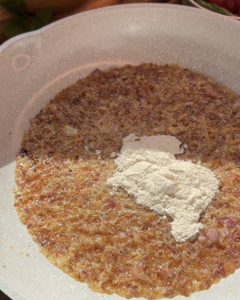 A pan with cooked onions and garlic, topped with flour, ready to create a creamy sauce.