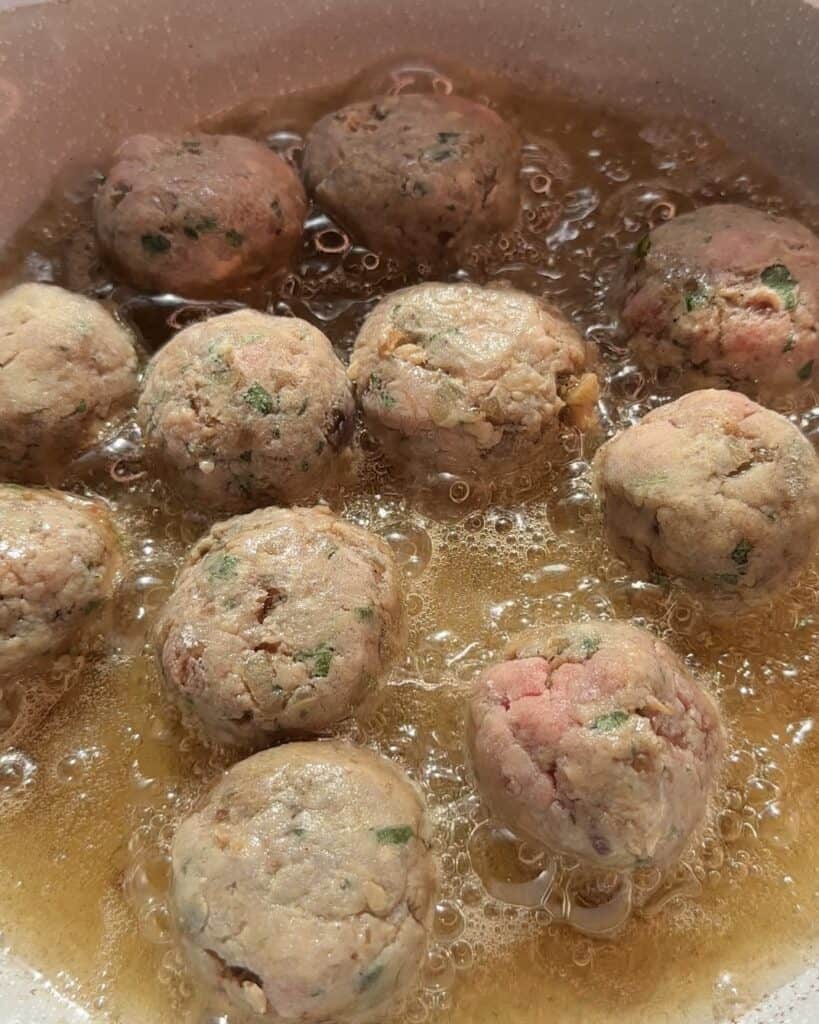 Juicy meatballs sizzling in a hot frying pan, turning golden brown as they cook, releasing rich aromas for a flavorful and hearty dish.