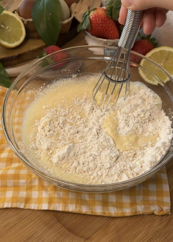 Whisking crepe batter in a bowl, incorporating flour for a smooth texture, essential for making soft strawberries and cream crepe rolls.