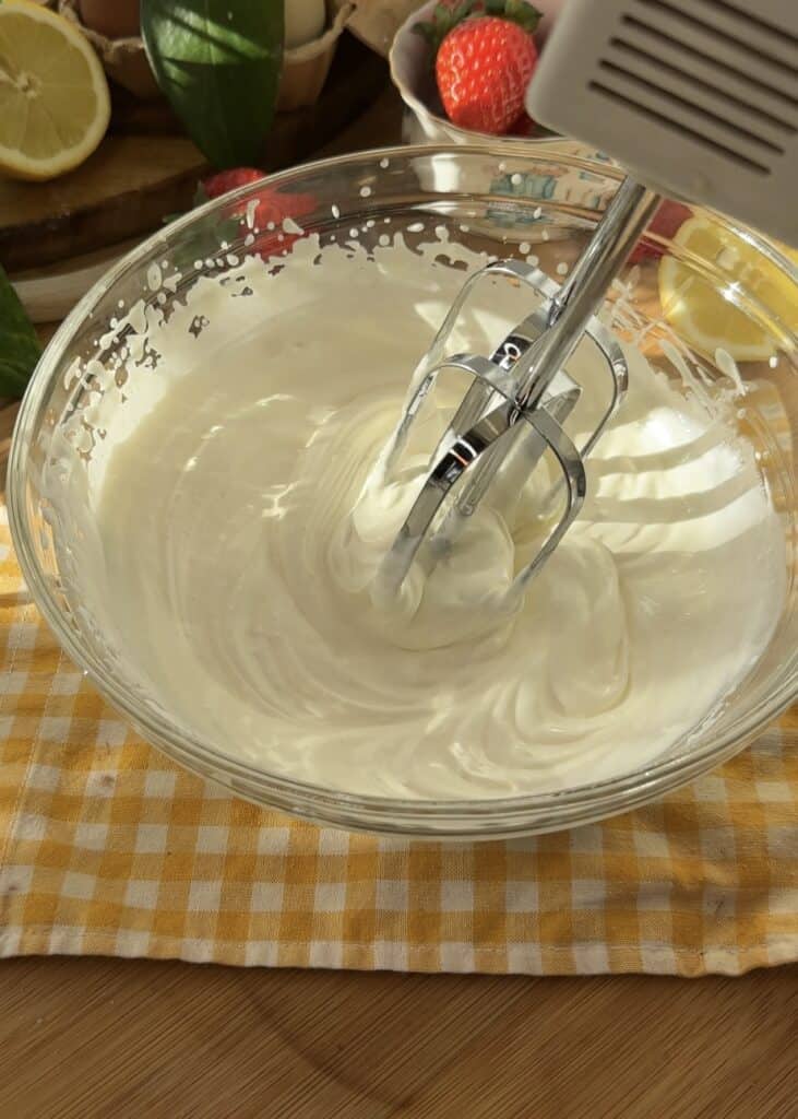 Fluffy whipped cream in a bowl being whipped with an electric mixer.