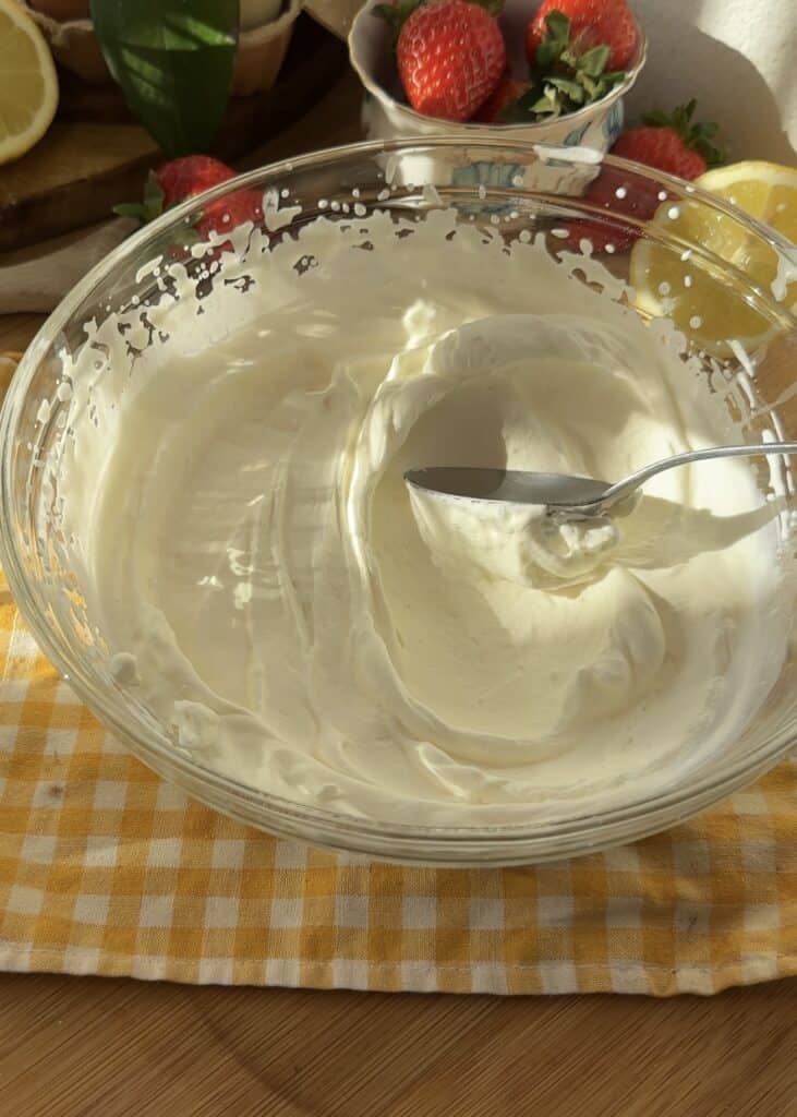 A spoon swirling through fluffy homemade whipped cream in a bowl, the perfect light and airy filling for strawberries and cream crepe rolls.