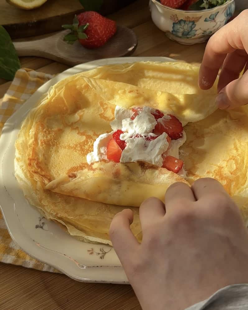 A close-up of a sweet crepe roll filled with fluffy whipped cream and fresh strawberries, showcasing its soft texture and creamy filling.