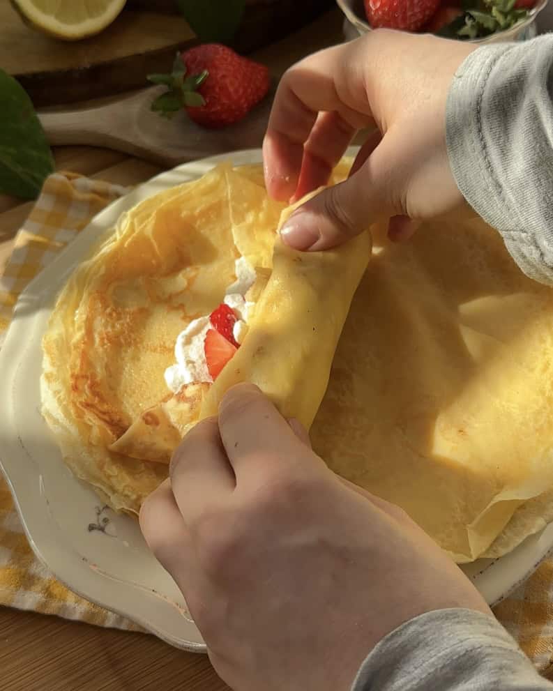 Close-up of a sweet crepe roll filled with whipped cream and fresh strawberries.