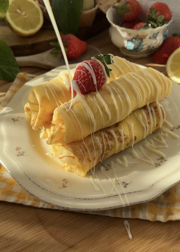 Delicious strawberries and cream crepe rolls drizzled with condensed milk, filled with fresh strawberries and homemade whipped cream, perfect for a sweet breakfast or dessert.