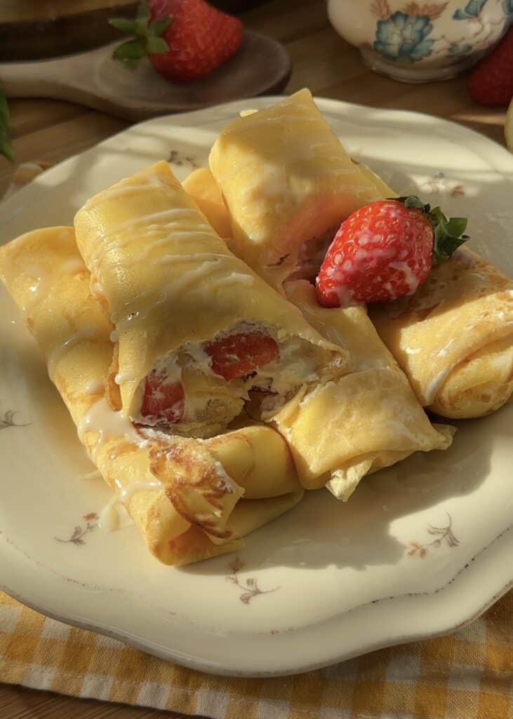 A bite taken from a strawberries and cream crepe roll, showing the delicious filling of whipped cream and fresh strawberries inside.