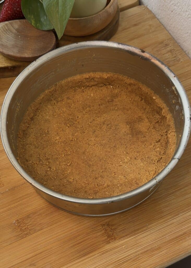Pressed pistachio cheesecake crust in a pan, ready to be frozen for a firm and stable base.