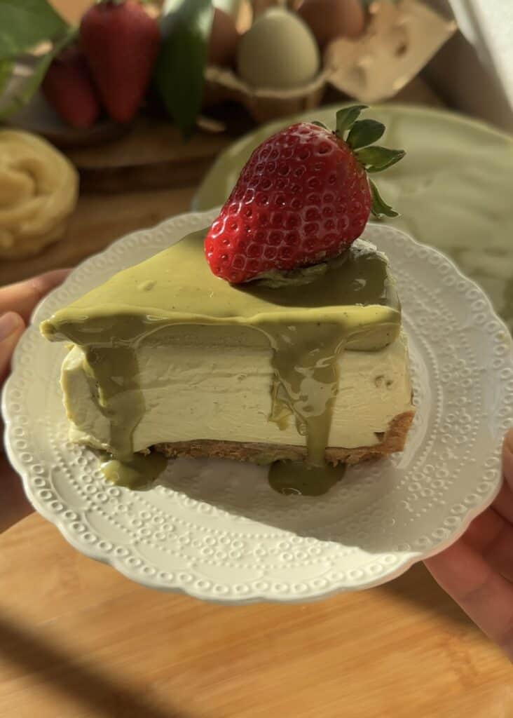 No-bake pistachio cheesecake slice with a creamy pistachio filling, crunchy crust, and topped with pistachio cream and a fresh strawberry