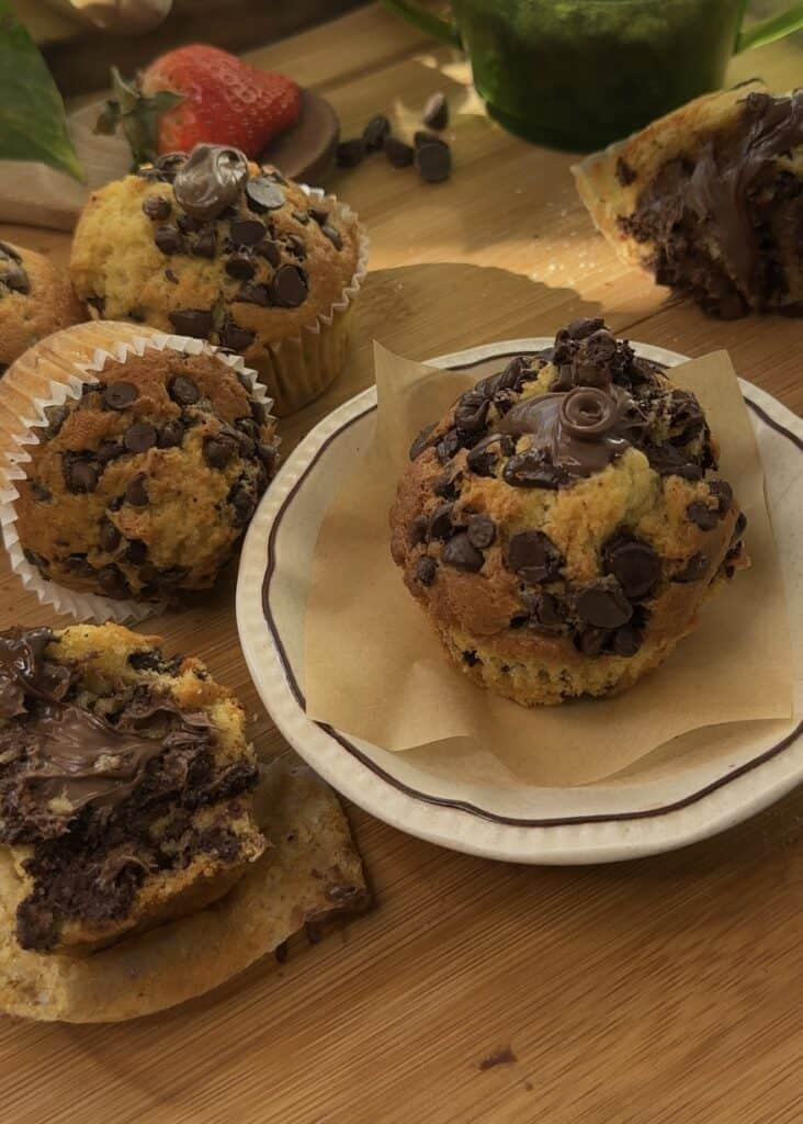 Nutella stuffed muffins on a wooden board with chocolate chips and Nutella on top.