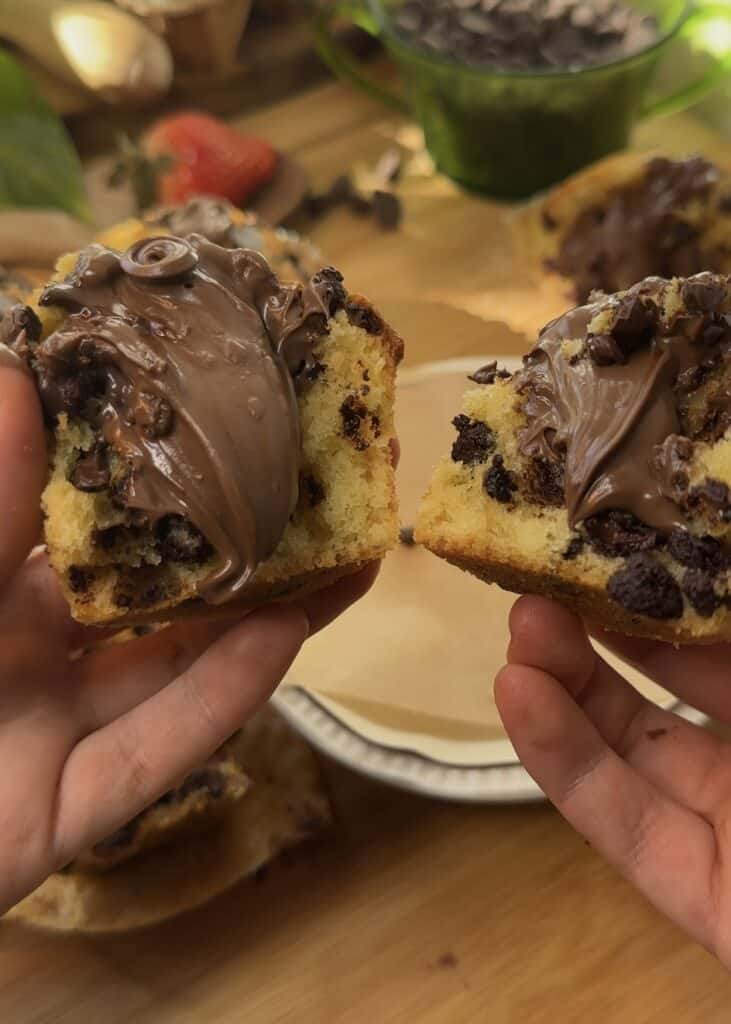 Freshly baked Nutella muffins opened in half, showing chocolate chips and oozing Nutella filling.