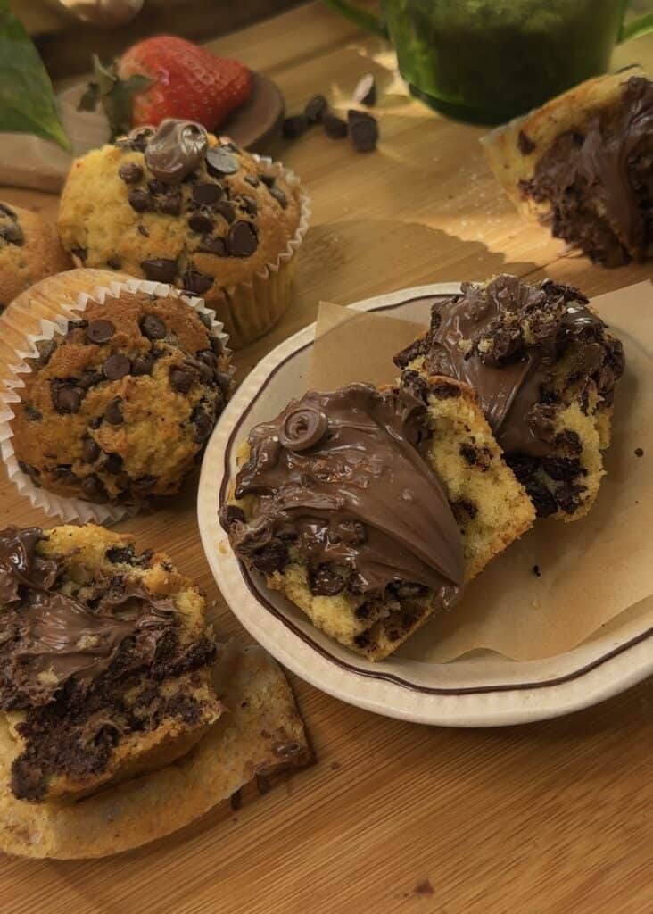 Nutella stuffed muffin oozing with chocolate hazelnut spread surrounded by chocolate chip muffins on a wooden board.