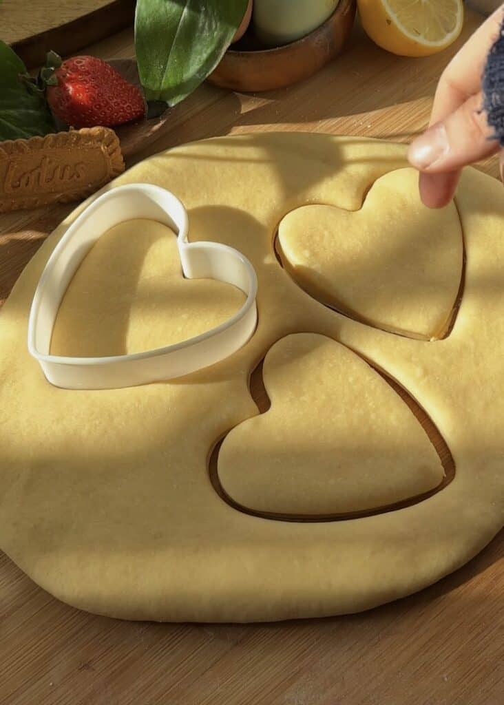 Cutting rolled-out dough with a heart-shaped cutter for Nutella heart donuts, perfect for Valentine’s Day desserts.