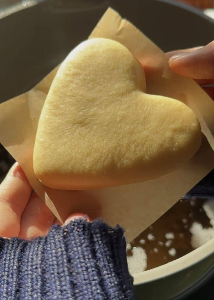Soft heart-shaped Nutella donut held in hand, ready to fry.
