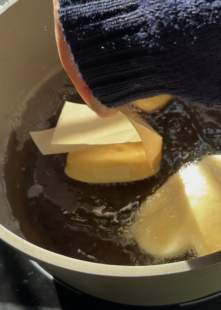 Gently dropping heart-shaped Nutella donuts into hot oil using baking paper for safe frying, a Valentine’s Day dessert.