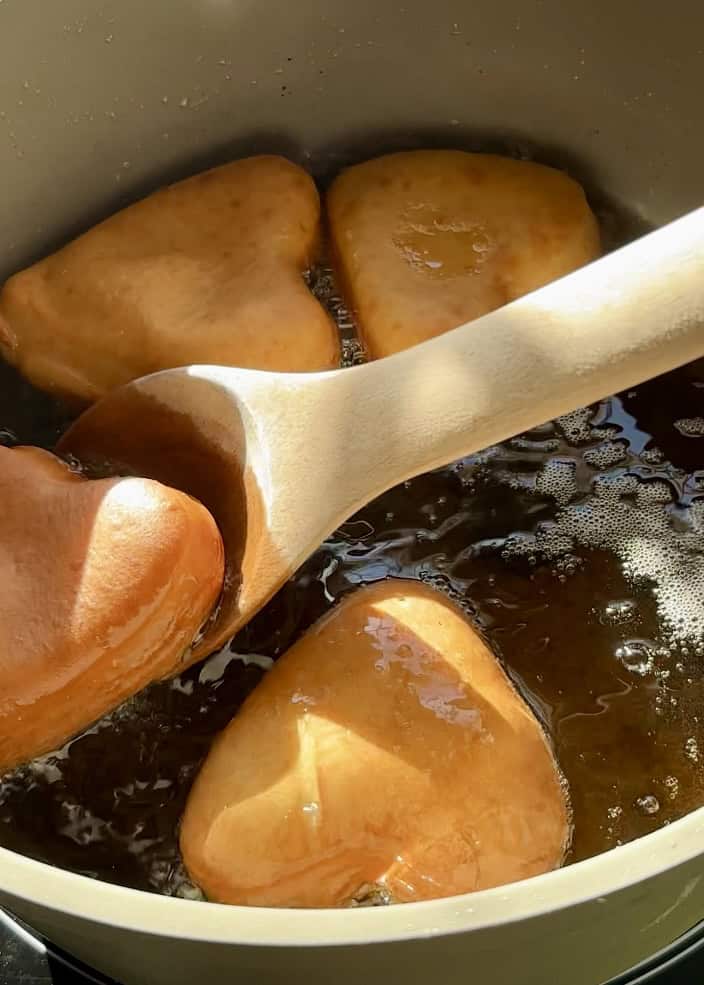 Frying heart-shaped Nutella donuts in hot oil using a wooden spoon for Valentine’s Day treats.